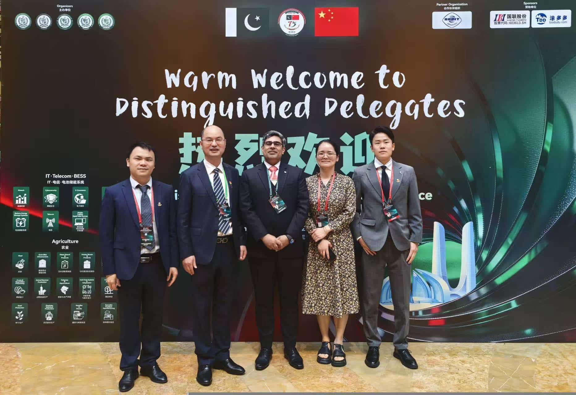 The image shows a group of people, possibly dignitaries, standing in front of a banner that includes a welcome message for distinguished delegates, and various logos and sponsor names, suggesting a conference or event related to technology and telecommunications.
AI-generated content may be incorrect.